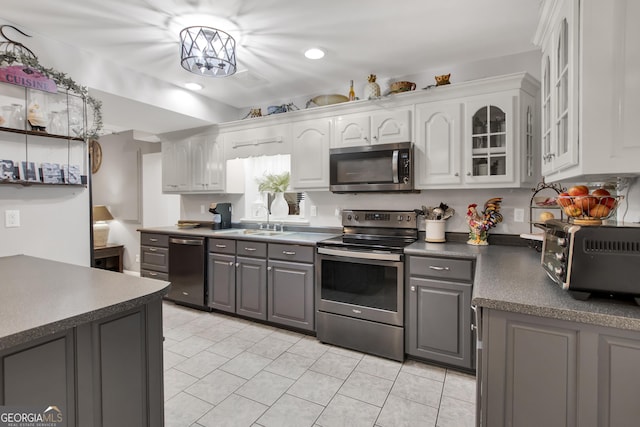 kitchen with a toaster, dark countertops, gray cabinetry, appliances with stainless steel finishes, and a sink