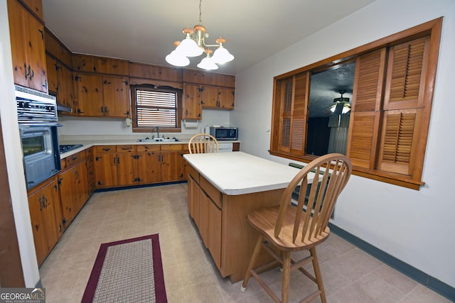 kitchen featuring pendant lighting, ceiling fan with notable chandelier, sink, black oven, and a kitchen island