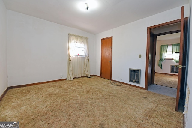 empty room with a fireplace, a healthy amount of sunlight, light carpet, and heating unit