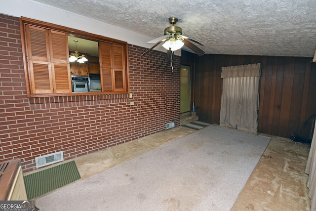 interior space featuring wooden walls, ceiling fan with notable chandelier, brick wall, and a textured ceiling