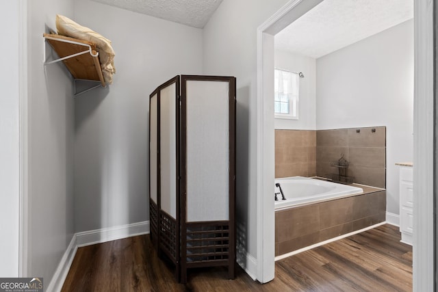 bathroom featuring hardwood / wood-style floors, a textured ceiling, and tiled bath