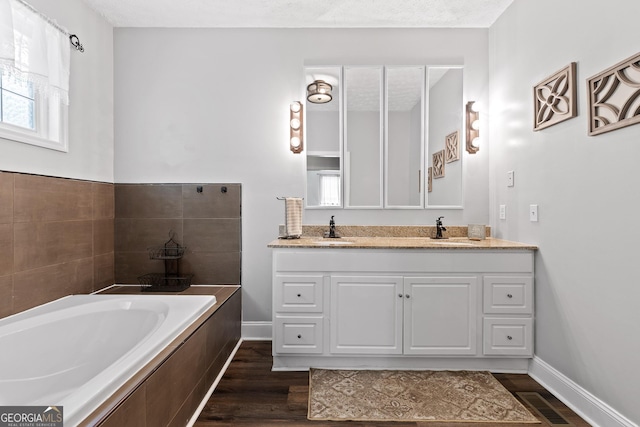 bathroom with hardwood / wood-style floors, vanity, a relaxing tiled tub, and a textured ceiling