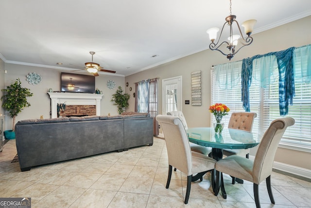 tiled dining space featuring ceiling fan with notable chandelier, a stone fireplace, and crown molding