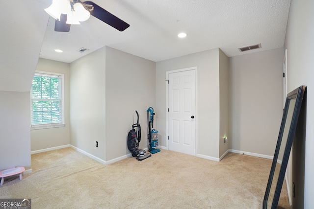 unfurnished room with a textured ceiling, ceiling fan, and light carpet