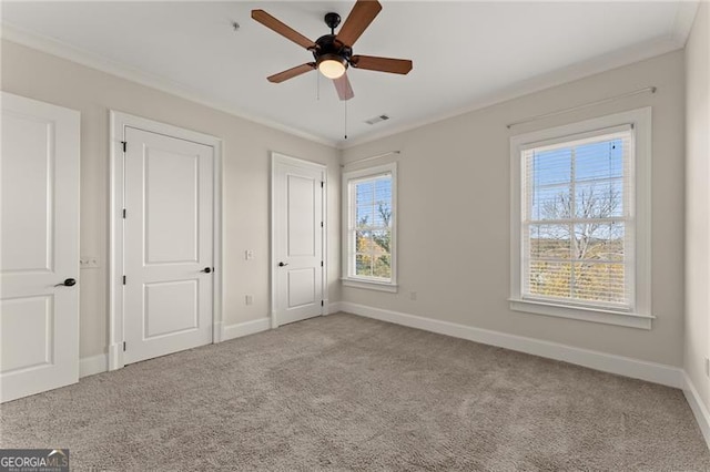 unfurnished bedroom with crown molding, light colored carpet, ceiling fan, and two closets