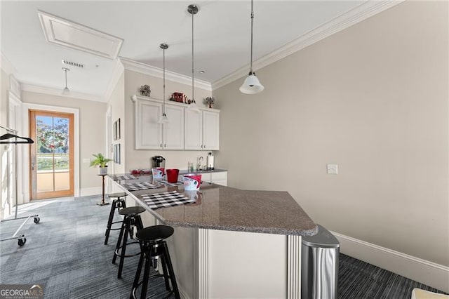 kitchen featuring a breakfast bar, crown molding, dark carpet, pendant lighting, and white cabinets