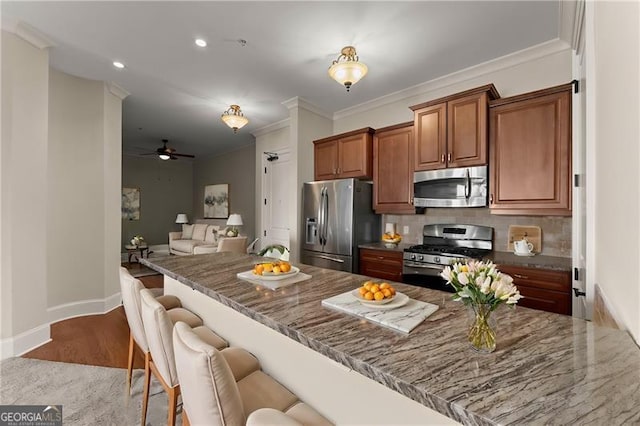 kitchen featuring appliances with stainless steel finishes, a breakfast bar, backsplash, crown molding, and light hardwood / wood-style flooring