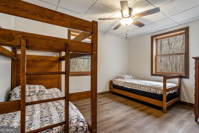 bedroom featuring multiple windows, wood-type flooring, a drop ceiling, and ceiling fan