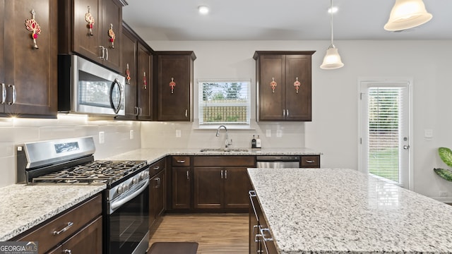 kitchen featuring decorative light fixtures, light stone counters, sink, and appliances with stainless steel finishes