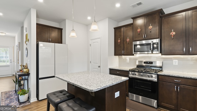 kitchen featuring pendant lighting, a kitchen island, appliances with stainless steel finishes, tasteful backsplash, and light hardwood / wood-style floors