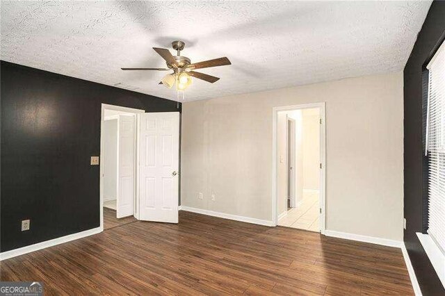 unfurnished bedroom featuring a textured ceiling, ceiling fan, ensuite bathroom, and dark wood-type flooring