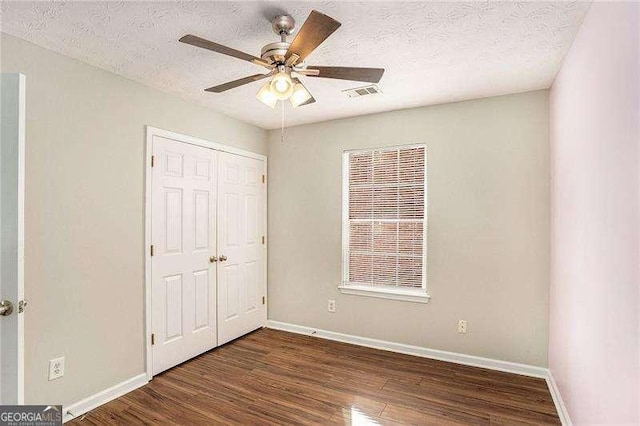 unfurnished bedroom with ceiling fan, dark hardwood / wood-style flooring, a textured ceiling, and a closet