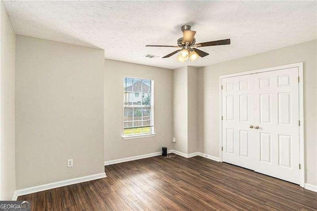 unfurnished bedroom with a textured ceiling, dark hardwood / wood-style flooring, a closet, and ceiling fan