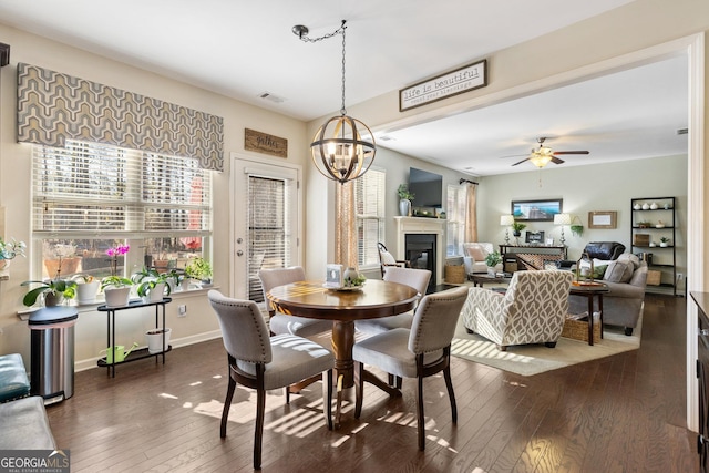 dining room featuring dark wood-type flooring, a wealth of natural light, and ceiling fan with notable chandelier