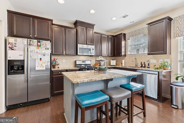 kitchen featuring sink, dark wood-type flooring, appliances with stainless steel finishes, a kitchen breakfast bar, and a kitchen island