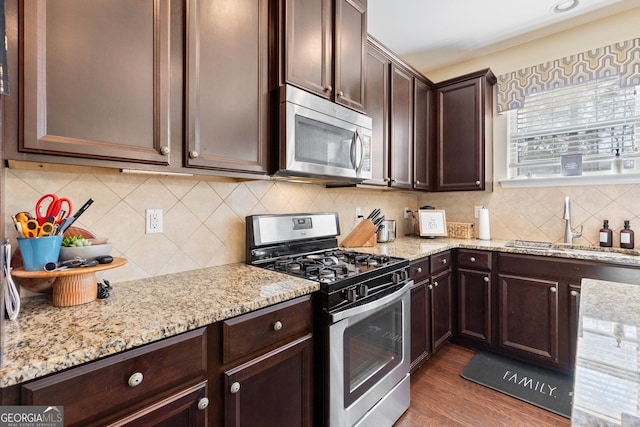 kitchen featuring dark wood-type flooring, sink, light stone counters, appliances with stainless steel finishes, and decorative backsplash