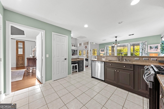 kitchen featuring light tile patterned flooring, dishwasher, light stone counters, gas range, and dark brown cabinets