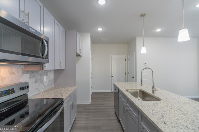 kitchen with light stone countertops, sink, hanging light fixtures, dark hardwood / wood-style flooring, and appliances with stainless steel finishes