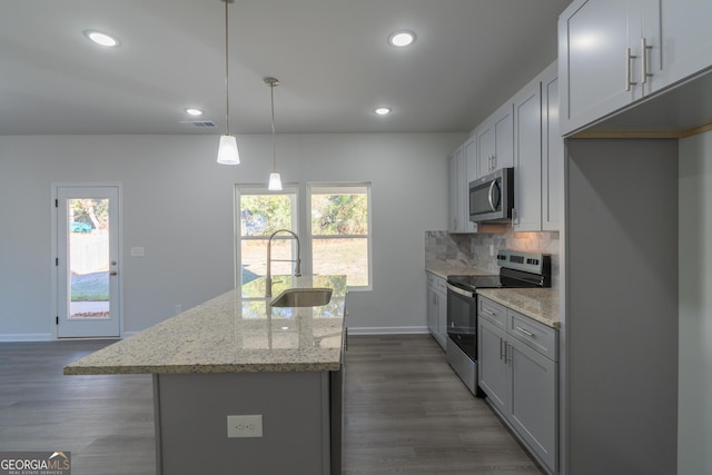 kitchen with a center island with sink, backsplash, appliances with stainless steel finishes, dark wood-type flooring, and a sink