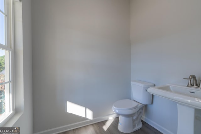 bathroom with baseboards, wood finished floors, toilet, and a healthy amount of sunlight