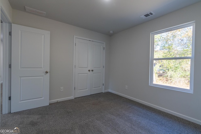 unfurnished bedroom with multiple windows, a closet, and dark carpet