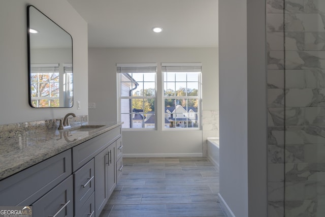 bathroom featuring recessed lighting, baseboards, a bath, and vanity