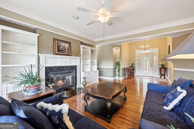 living room featuring hardwood / wood-style flooring, a high end fireplace, ceiling fan with notable chandelier, and ornamental molding