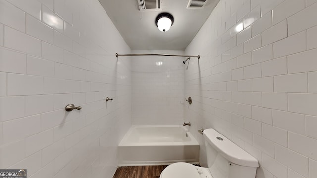 bathroom featuring hardwood / wood-style flooring, toilet, tiled shower / bath, and tile walls