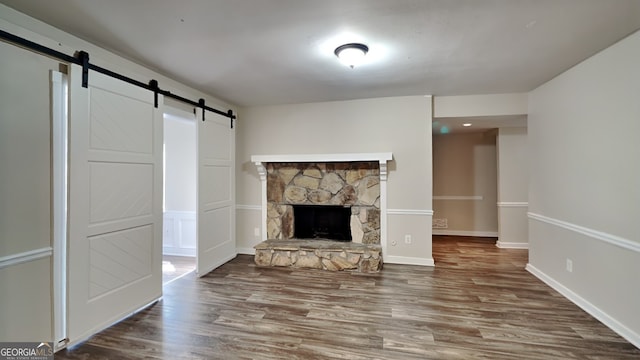 unfurnished living room featuring a barn door, a stone fireplace, and wood-type flooring