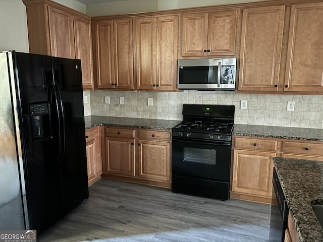 kitchen with black appliances, backsplash, hardwood / wood-style floors, and dark stone counters