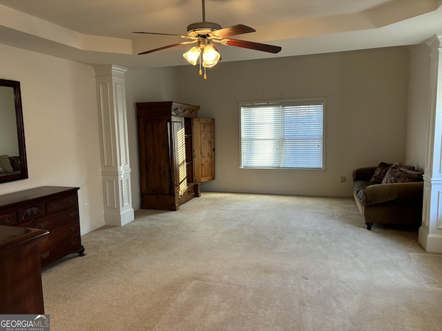 sitting room with a raised ceiling, ornate columns, light carpet, and ceiling fan