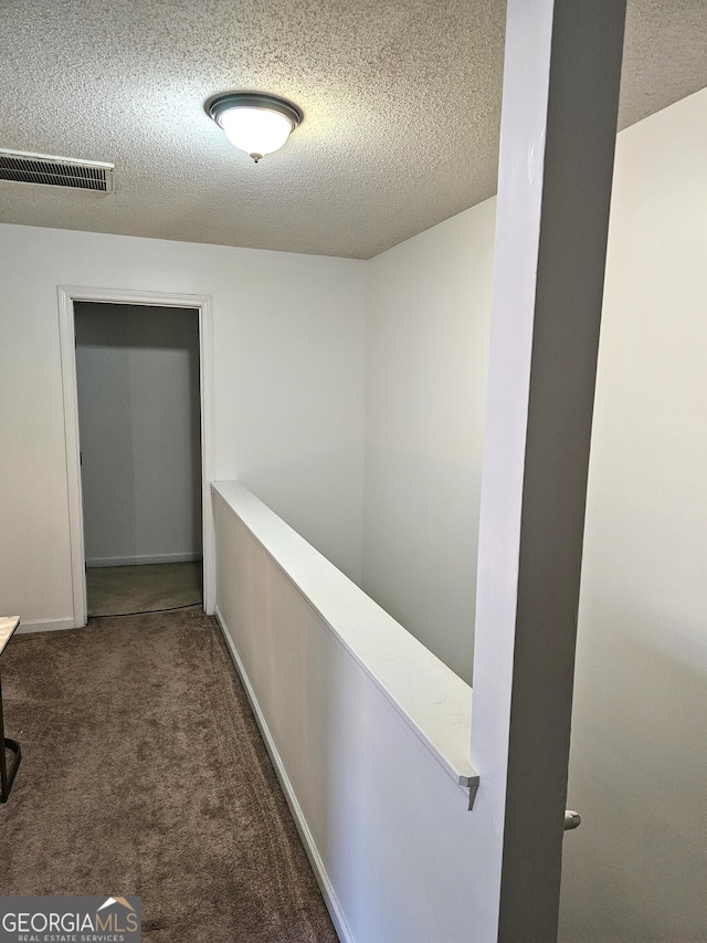 corridor with dark colored carpet and a textured ceiling