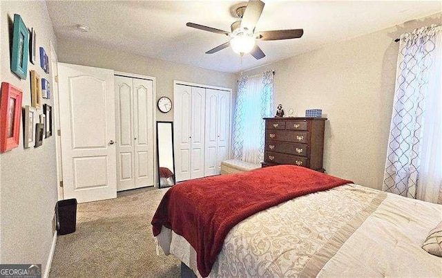 bedroom with two closets, light colored carpet, and ceiling fan