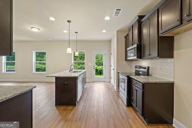 kitchen featuring appliances with stainless steel finishes, decorative light fixtures, light stone counters, and a healthy amount of sunlight