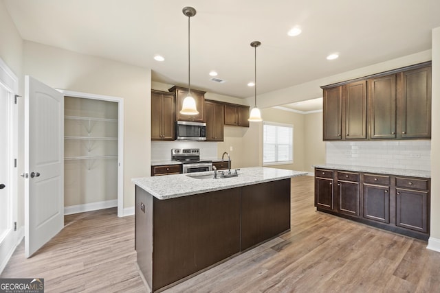 kitchen with light stone countertops, stainless steel appliances, sink, decorative light fixtures, and light hardwood / wood-style flooring