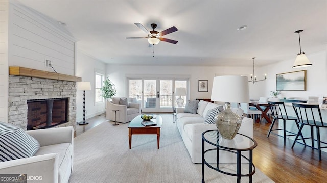 living room featuring ceiling fan with notable chandelier, a stone fireplace, and light hardwood / wood-style flooring