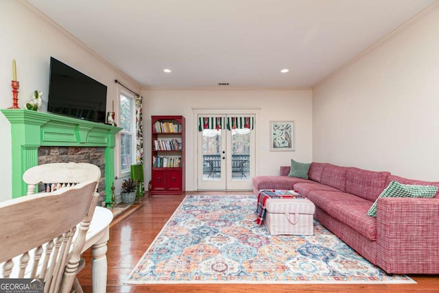 living room with ornamental molding, a stone fireplace, french doors, and hardwood / wood-style floors