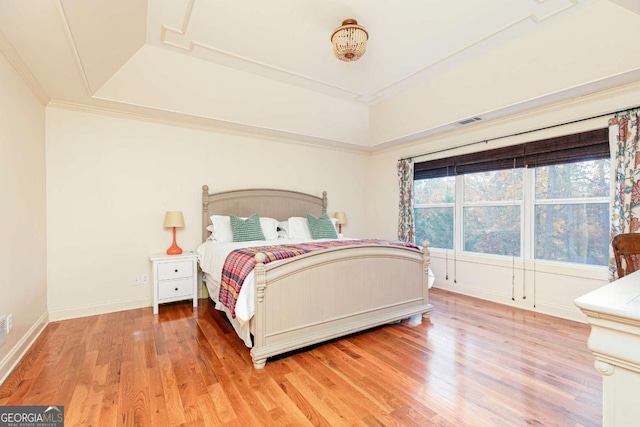 bedroom featuring wood-type flooring, ornamental molding, and a tray ceiling