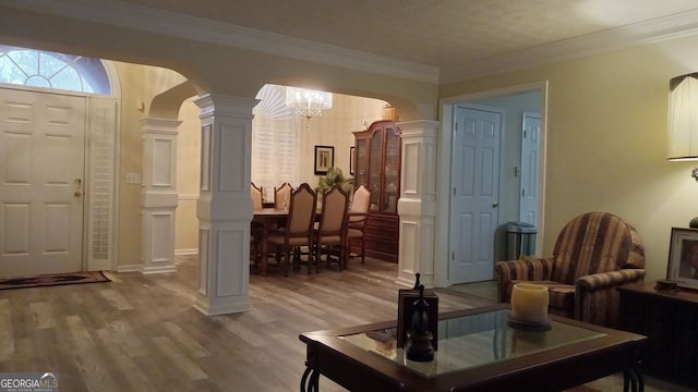 interior space featuring an inviting chandelier, hardwood / wood-style floors, crown molding, and decorative columns