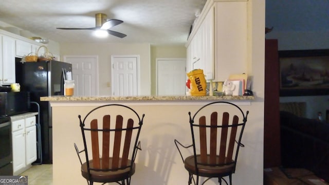 kitchen with a kitchen bar, white cabinets, light stone counters, and kitchen peninsula