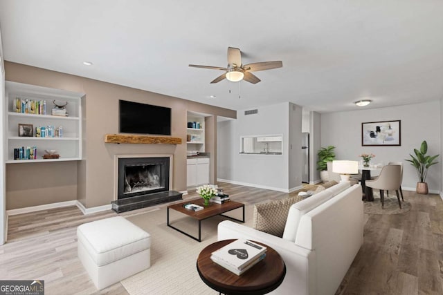 living room featuring built in shelves, ceiling fan, and light hardwood / wood-style floors