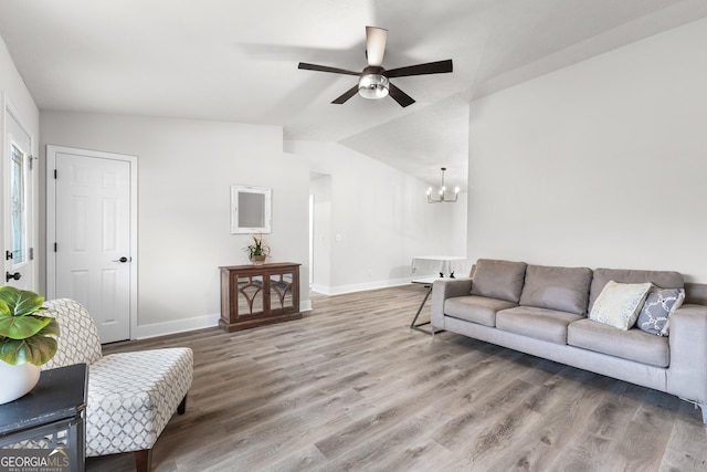 living room featuring ceiling fan with notable chandelier, hardwood / wood-style flooring, and vaulted ceiling