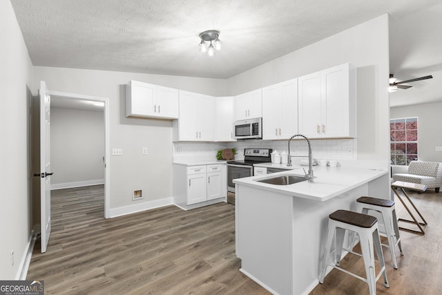 kitchen featuring sink, kitchen peninsula, dark hardwood / wood-style flooring, white cabinetry, and stainless steel appliances