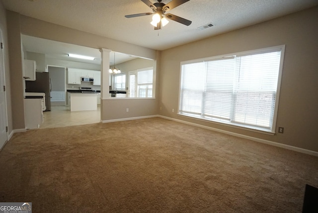 unfurnished living room with a textured ceiling, light carpet, ceiling fan with notable chandelier, visible vents, and baseboards