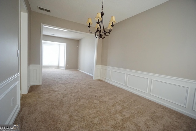 carpeted empty room featuring a wainscoted wall, visible vents, a decorative wall, and a chandelier