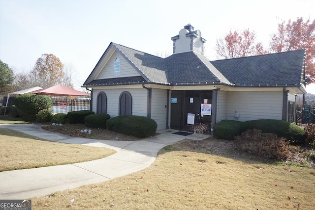 view of front facade featuring a shingled roof, a front yard, and fence