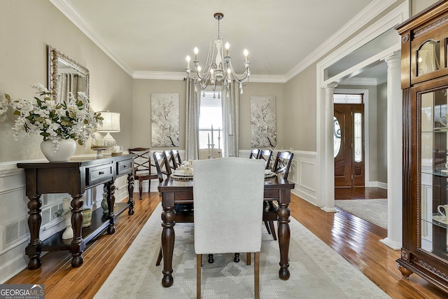 dining room with ornate columns, crown molding, an inviting chandelier, and light wood-type flooring