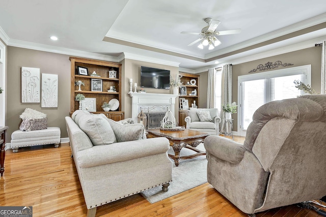 living room featuring ceiling fan, a raised ceiling, ornamental molding, and light hardwood / wood-style flooring