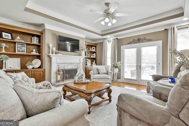 living room featuring french doors, ceiling fan, light wood-type flooring, ornamental molding, and a tray ceiling