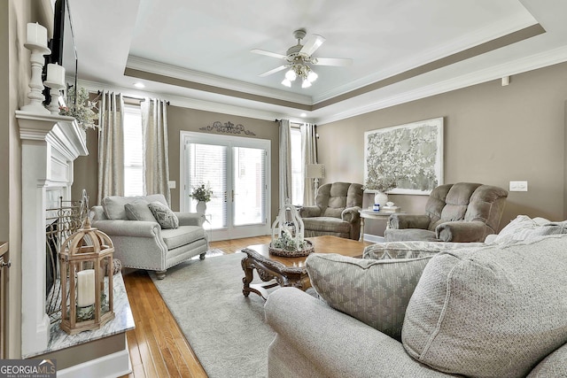 living room with ceiling fan, a raised ceiling, light wood-type flooring, and ornamental molding